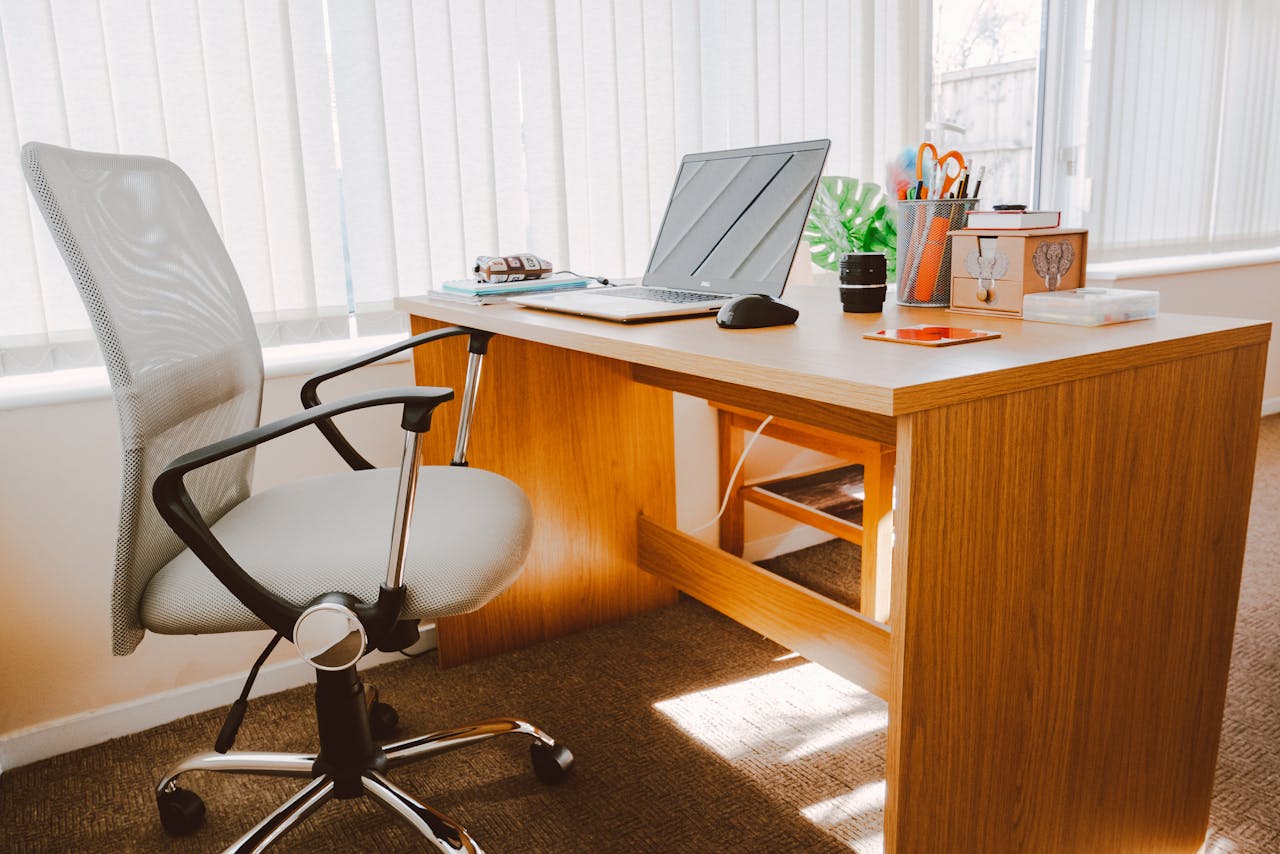 digital A modern office workspace featuring a wooden desk, chair, laptop, and bright natural light.